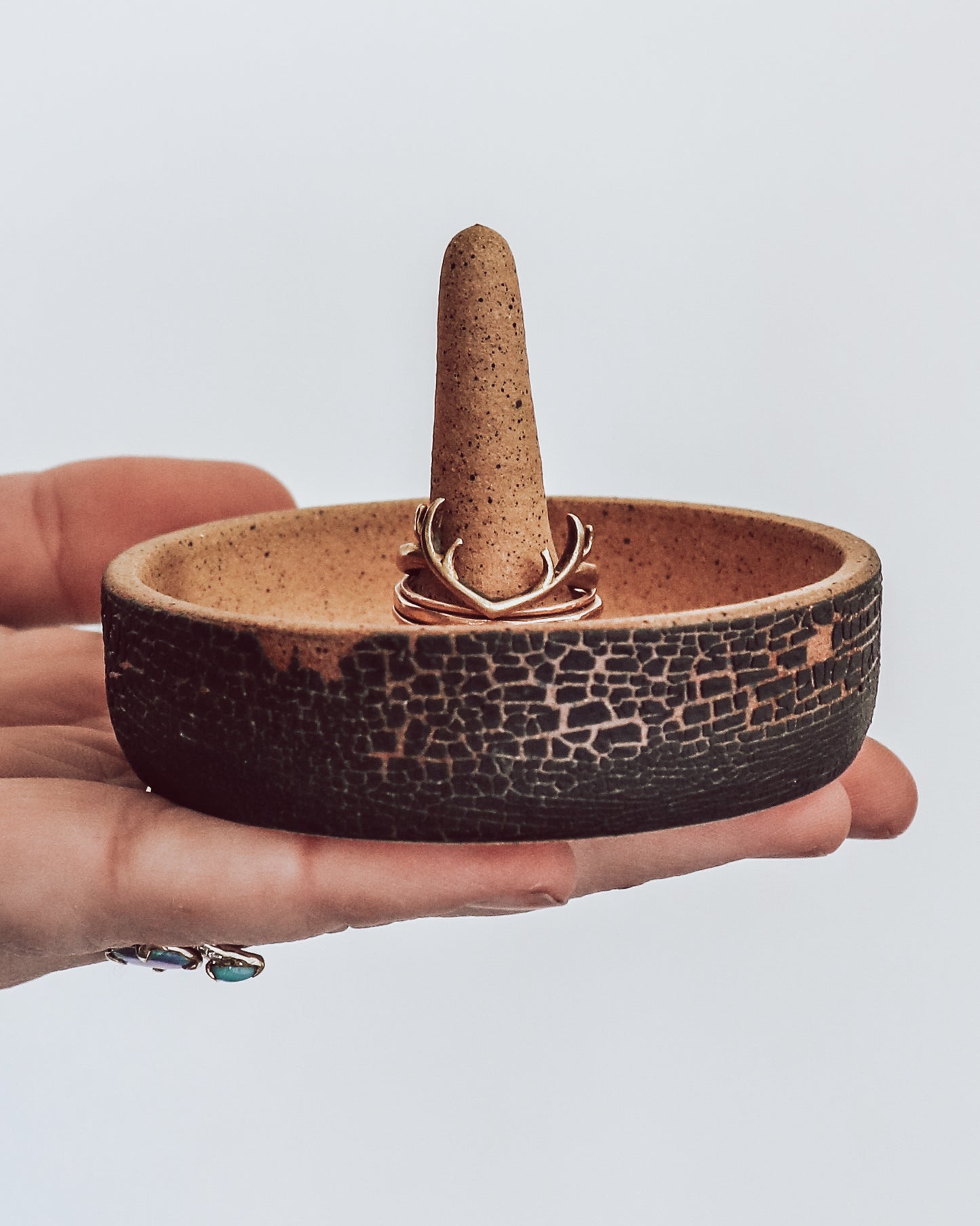 Hand holding a handmade ceramic ring holder dish with central cone. Exterior of dish has a dark textured exterior.