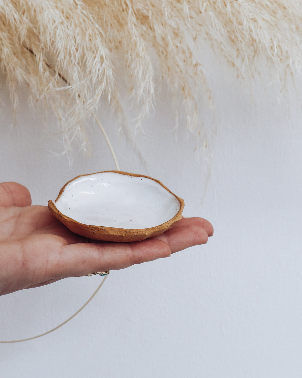 Stone Ring Dish in glossy white glaze with raw clay edge, shown held in hand for scale.