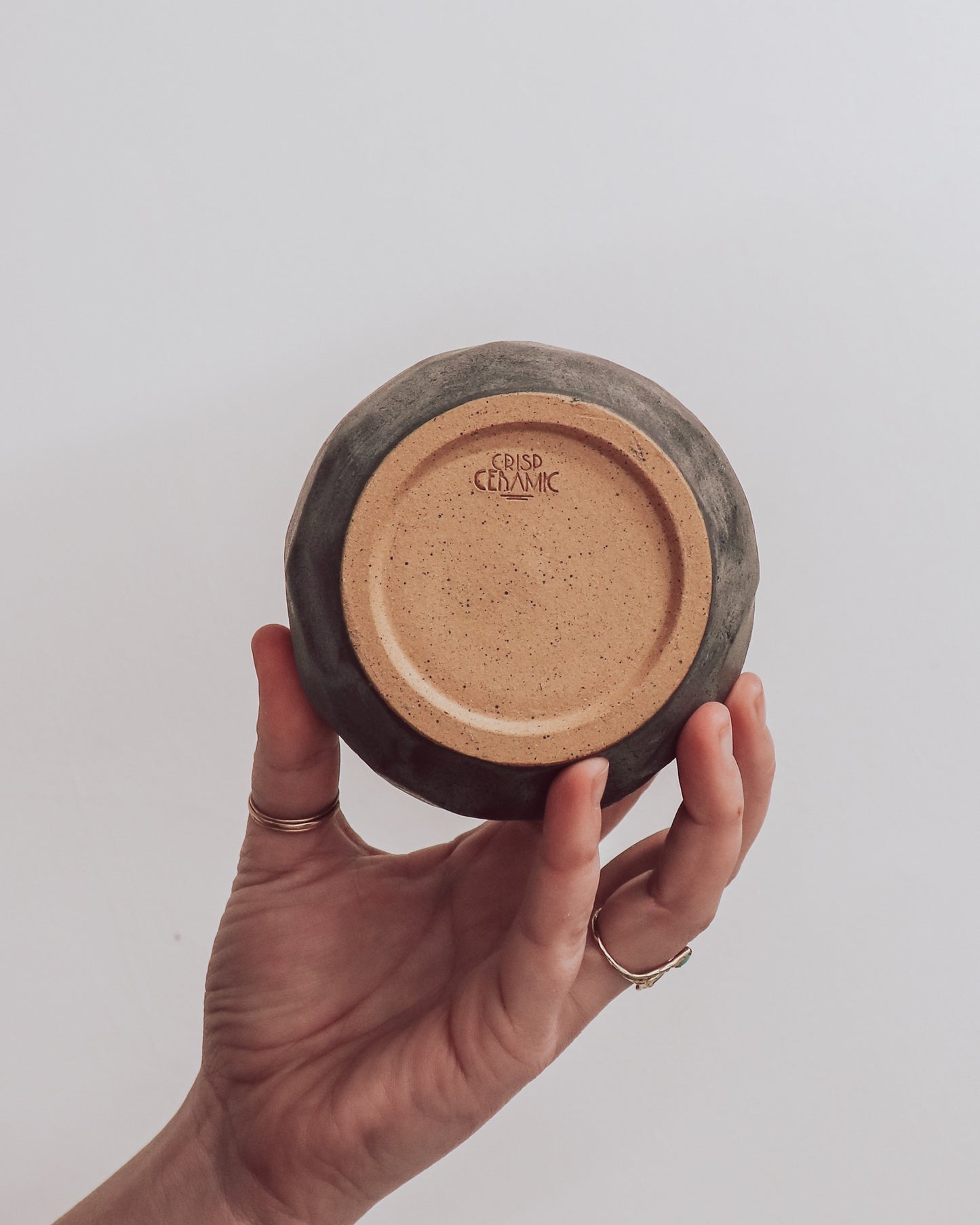 A ceramic 'boulder' planter or vase with a matte charcoal glaze, held in a person's hand showing crisp ceramic makers mark.