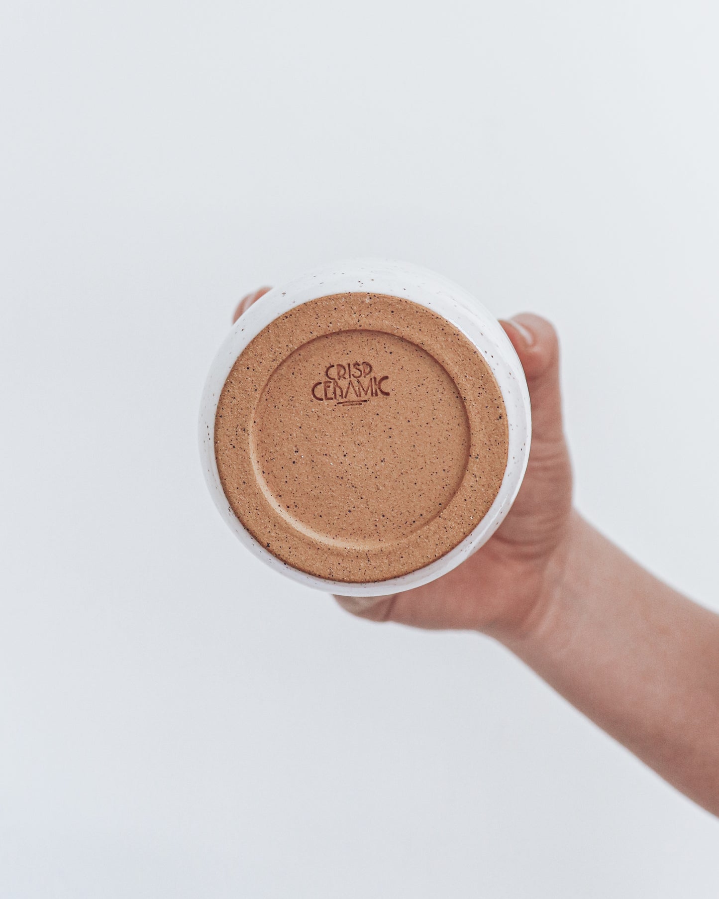 A ceramic fox-shaped tumbler with a glossy white glaze, held in a person's hand against a white background. shows unglazed bottom with crisp ceramic makers mark.