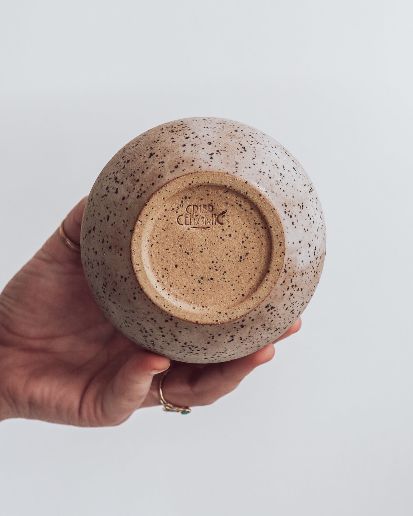 A hand holding a small brown and beige ceramic vase with a crackled texture and geometric patterns.shows unglazed bottom with crisp ceramic makers mark.