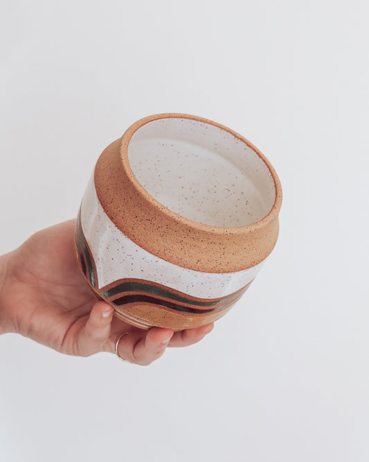 Hand holding a handmade ceramic planter with white glaze and wavy multicolored stripe detailing.