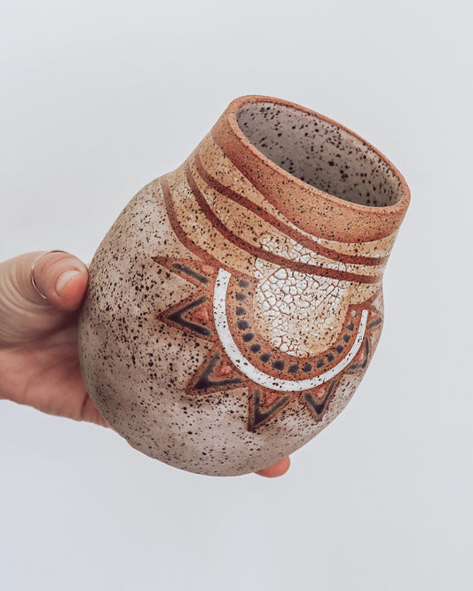 A hand holding a small brown and beige ceramic vase with a crackled texture and geometric patterns.