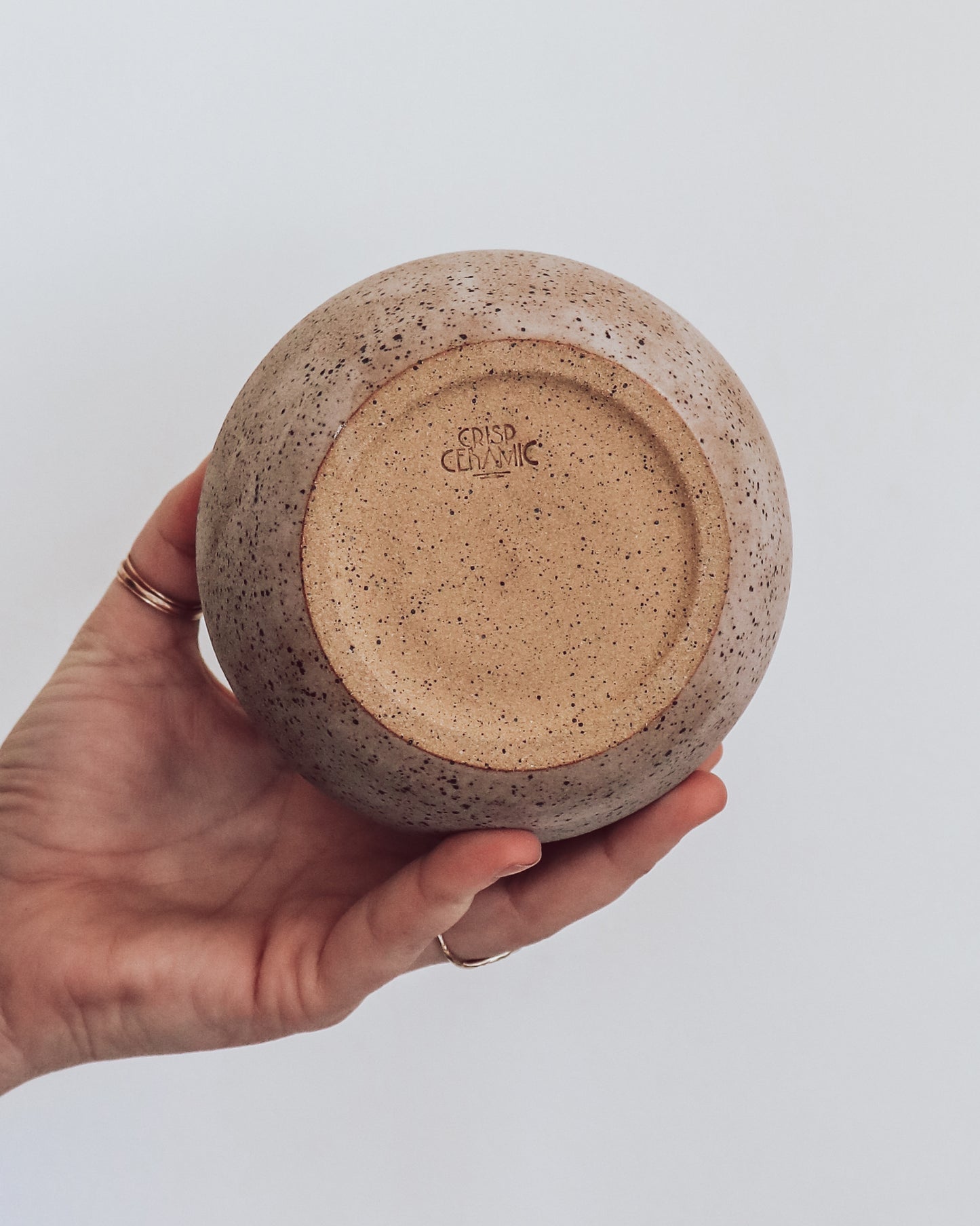 A hand holding a small brown and beige ceramic vase with a crackled texture and geometric patterns. Shows unglazed bottom of vase with crisp ceramic makers mark.