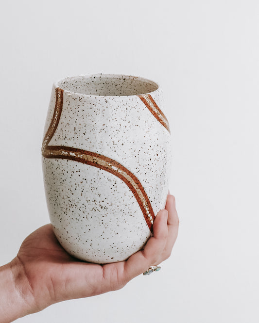 hand holding a handmade speckled ceramic tumbler with flowing carved brown line detailing.