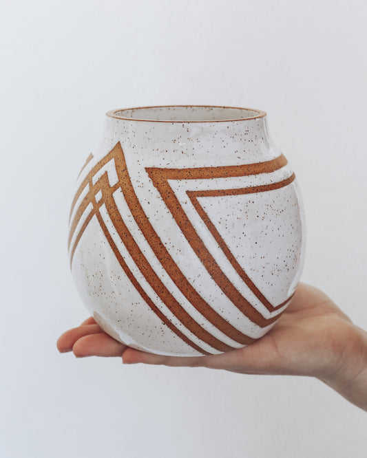 Hand holding a handmade speckled ceramic vase with geometric stripe detailing in warm brown tones.