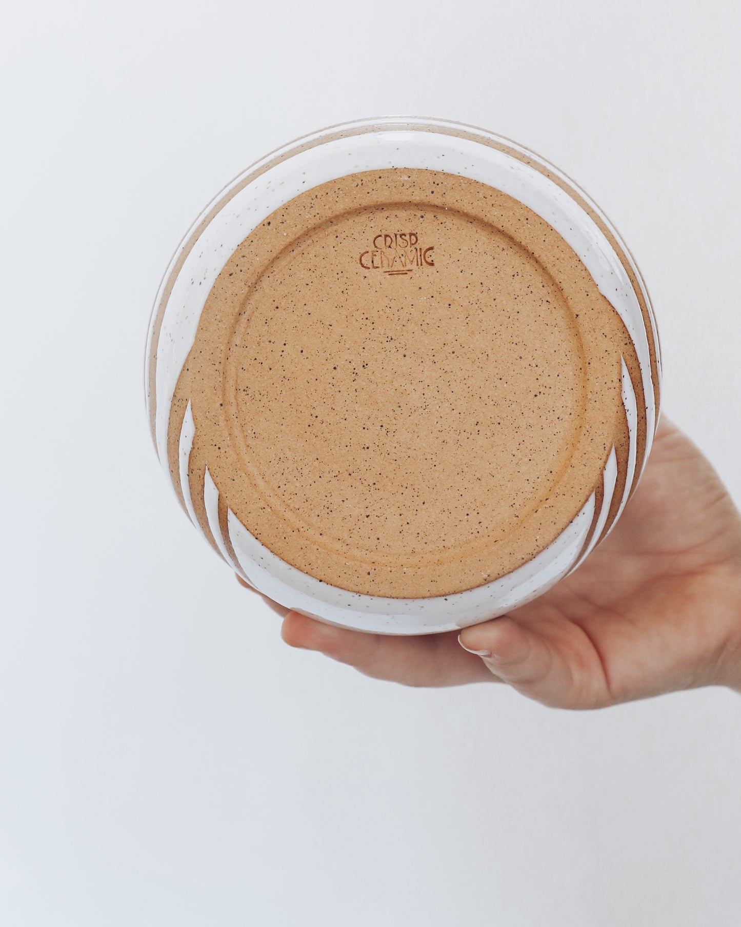 Hand holding a handmade speckled ceramic vase with geometric stripe detailing in warm brown tones. Unglazed underside shown with crisp ceramic makers mark.