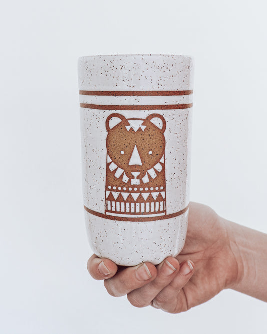 Hand Holding a handmade speckled ceramic tumbler featuring a brown illustrated bear design with geometric detailing.