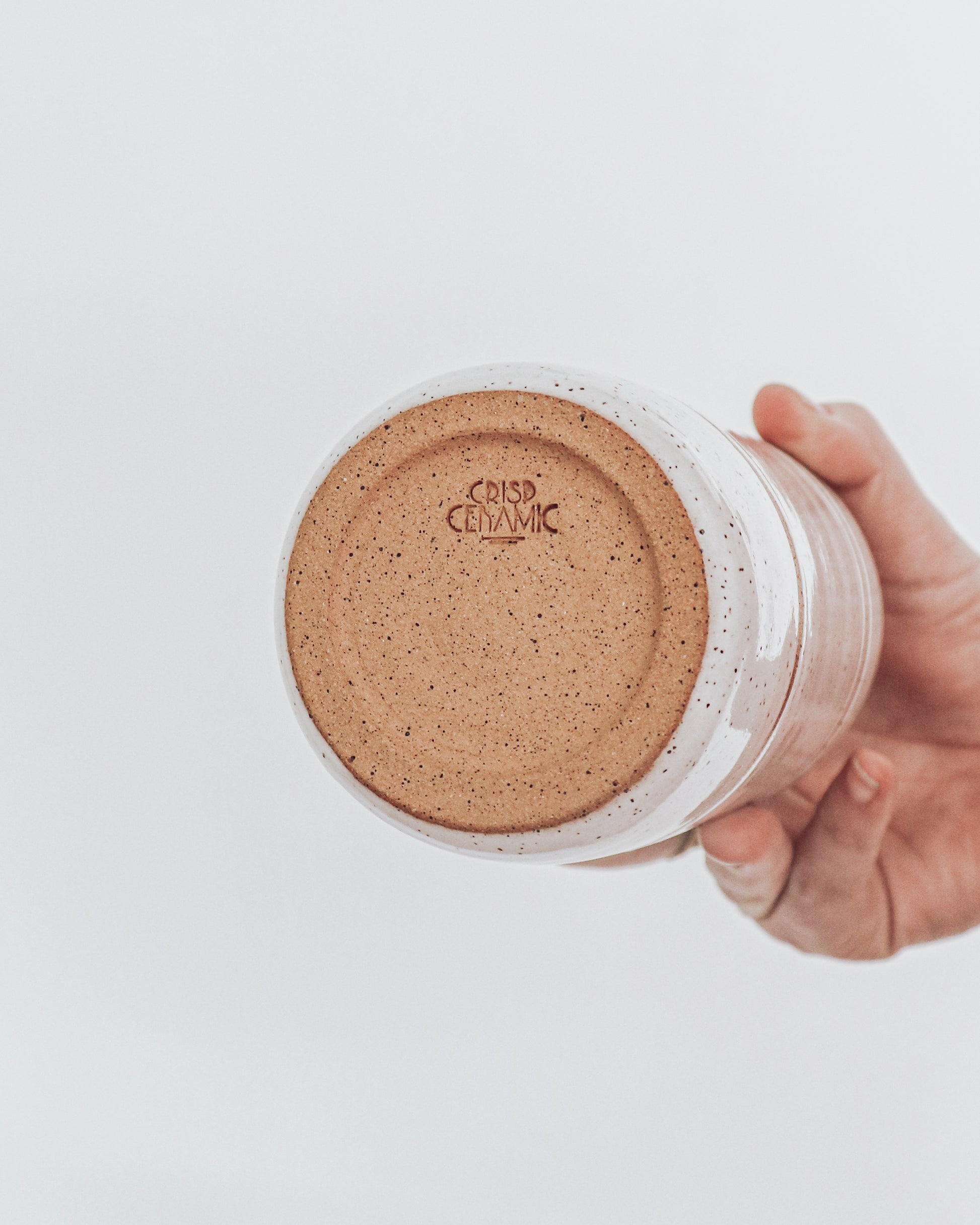 Hand holding underside of a handmade speckled ceramic cup showing the crisp ceramic makers stamp. 