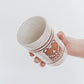 Inside view of Hand Holding a handmade speckled ceramic tumbler featuring a brown illustrated bear design with geometric detailing. 
