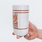 side view of Hand Holding a handmade speckled ceramic tumbler featuring a brown illustrated bear design with geometric detailing. 