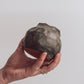 A ceramic 'boulder' planter or vase with a matte charcoal glaze, held in a person's hand.