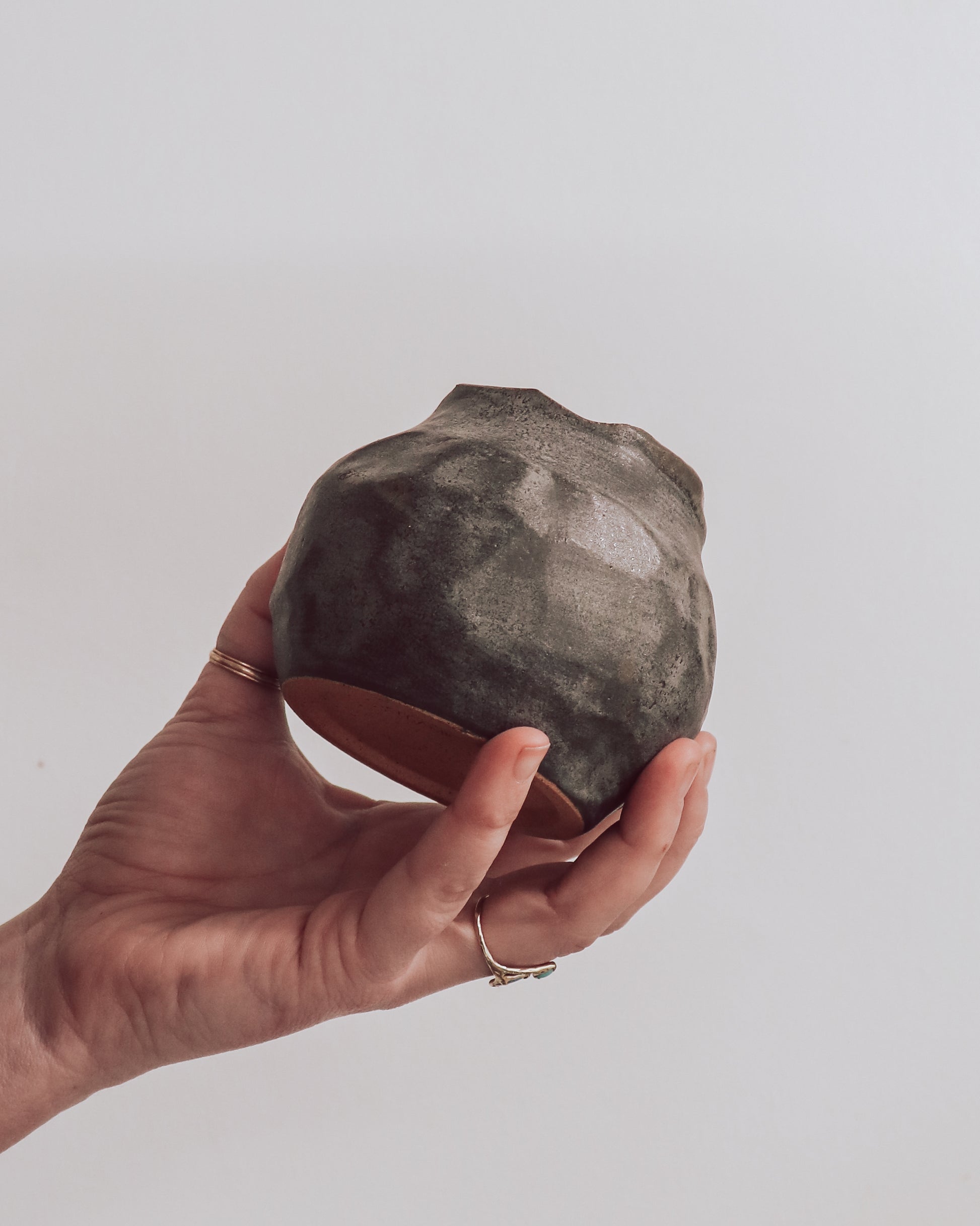 A ceramic 'boulder' planter or vase with a matte charcoal glaze, held in a person's hand.
