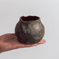 A ceramic 'boulder' planter or vase with a matte charcoal glaze, held in a person's hand.