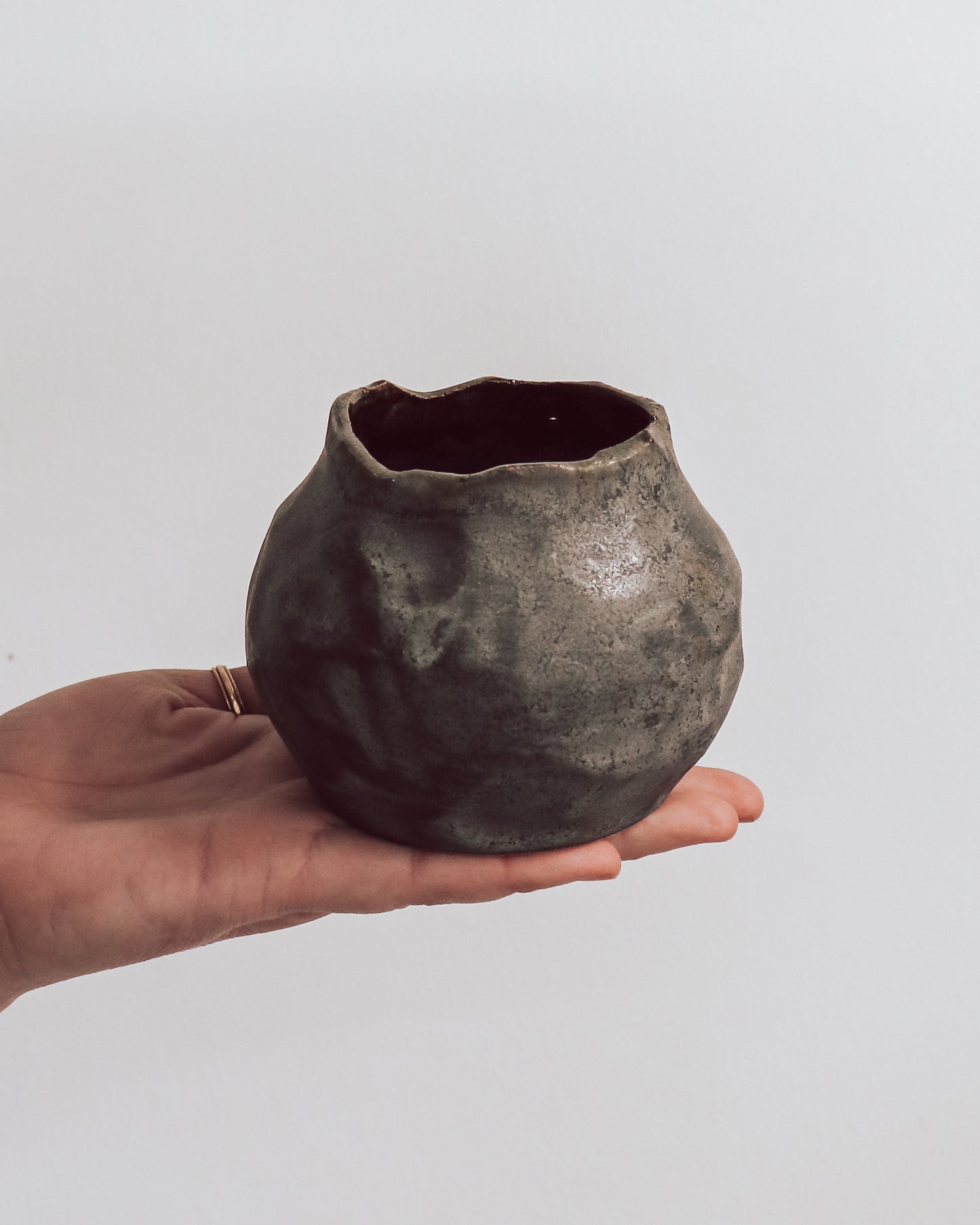 A ceramic 'boulder' planter or vase with a matte charcoal glaze, held in a person's hand.