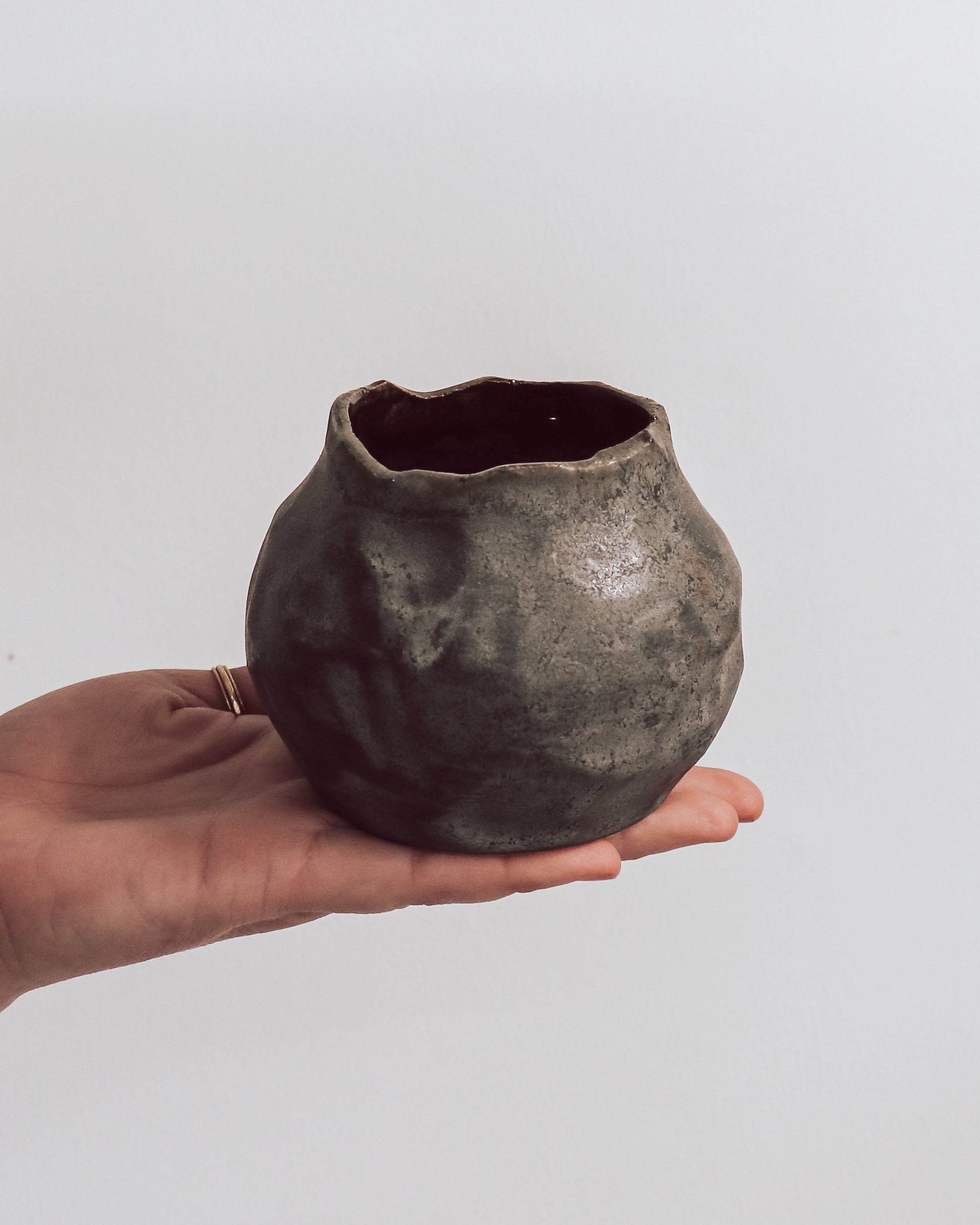 A ceramic 'boulder' planter or vase with a matte charcoal glaze, held in a person's hand.