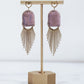 Ceramic and brass arch tassel earrings with gold fringe, shown in amethyst on a gold stand.