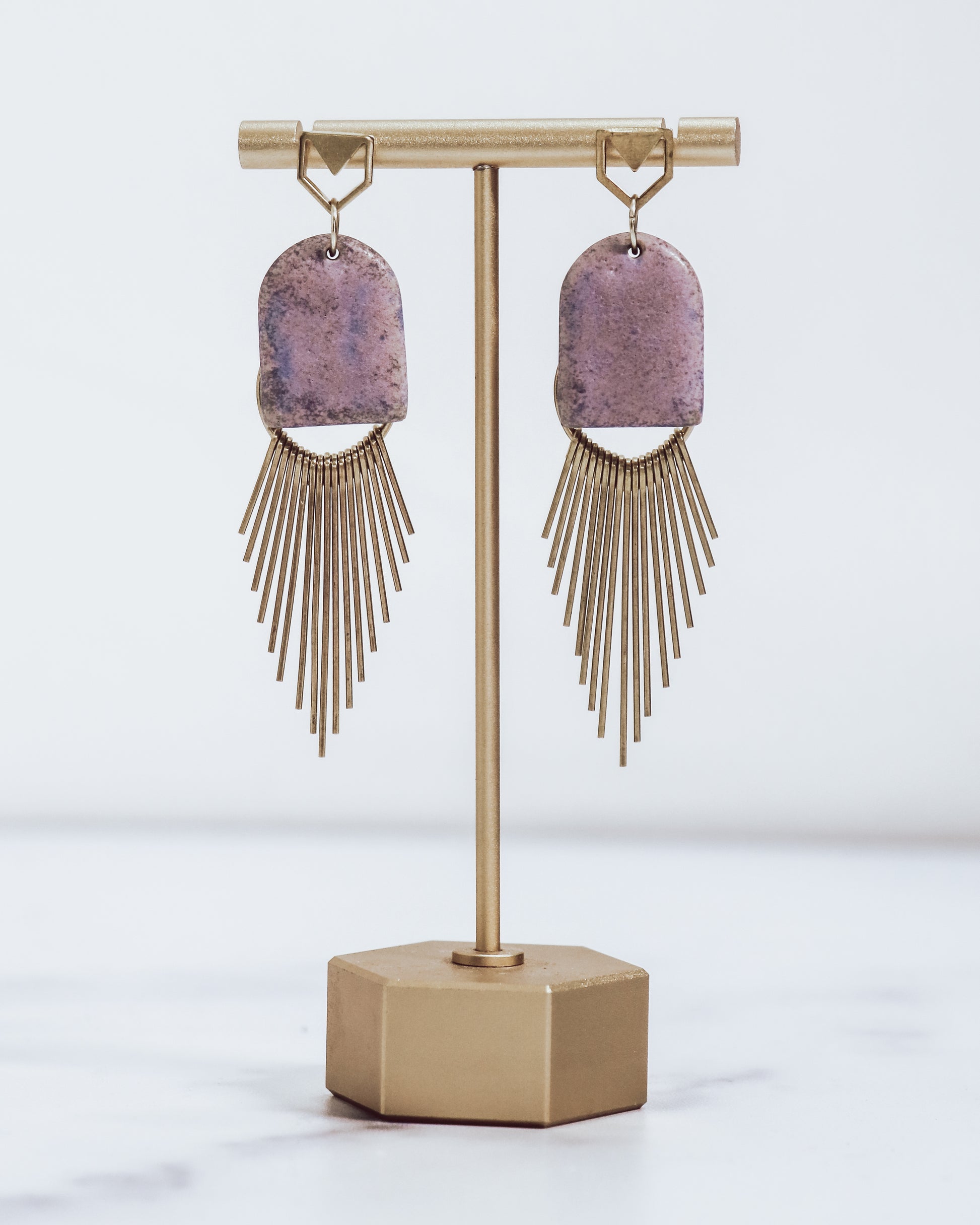 Ceramic and brass arch tassel earrings with gold fringe, shown in amethyst on a gold stand.