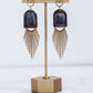 Ceramic and brass arch tassel earrings with gold fringe, shown in midnight blue on a gold stand.