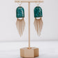 Ceramic and brass arch tassel earrings with gold fringe, shown in turquoise on a gold stand.