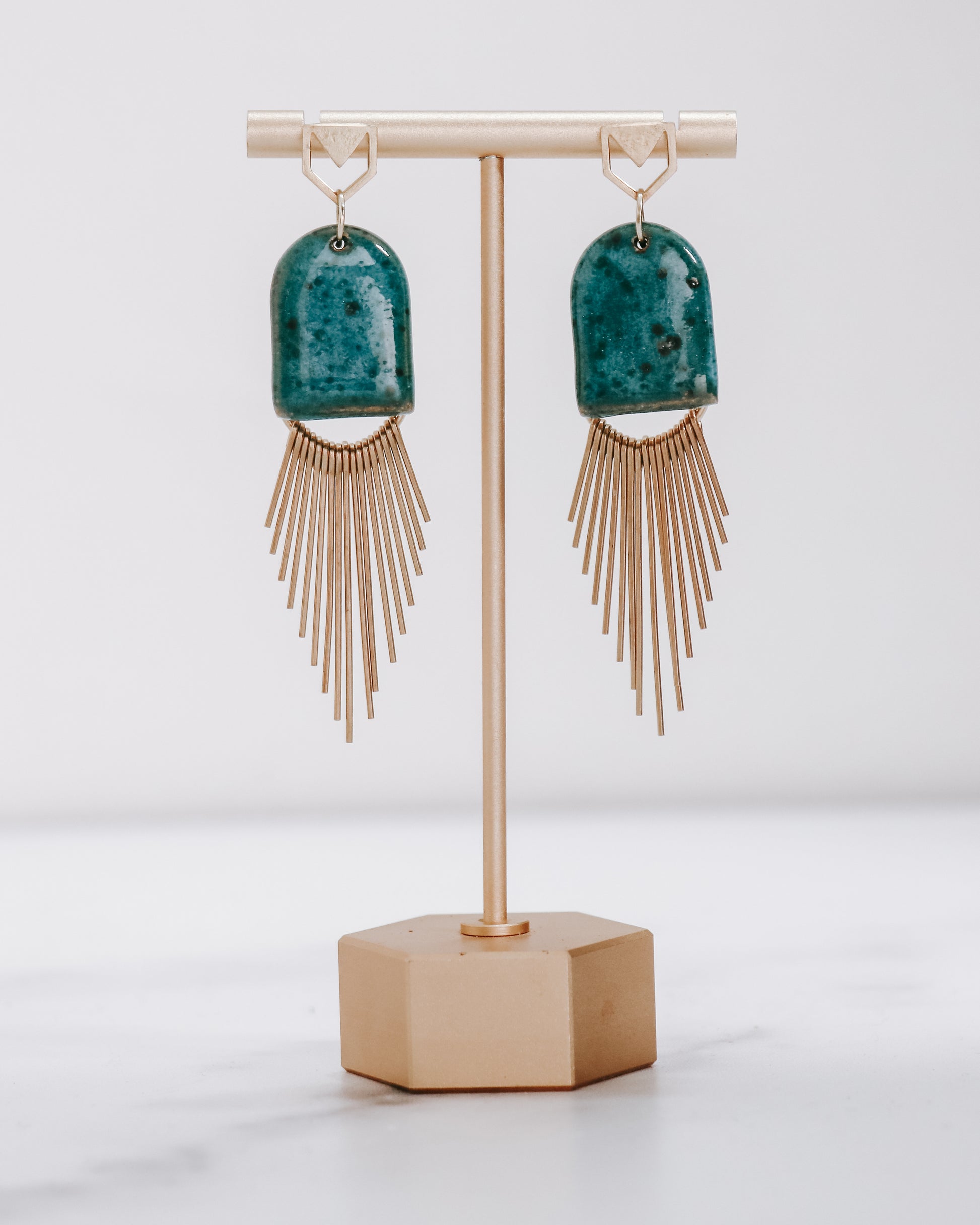 Ceramic and brass arch tassel earrings with gold fringe, shown in turquoise on a gold stand.