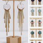 Long gold fringe tassel earrings with hexagon-shaped ceramic tops, shown in multiple glaze color options on a gold stand. 