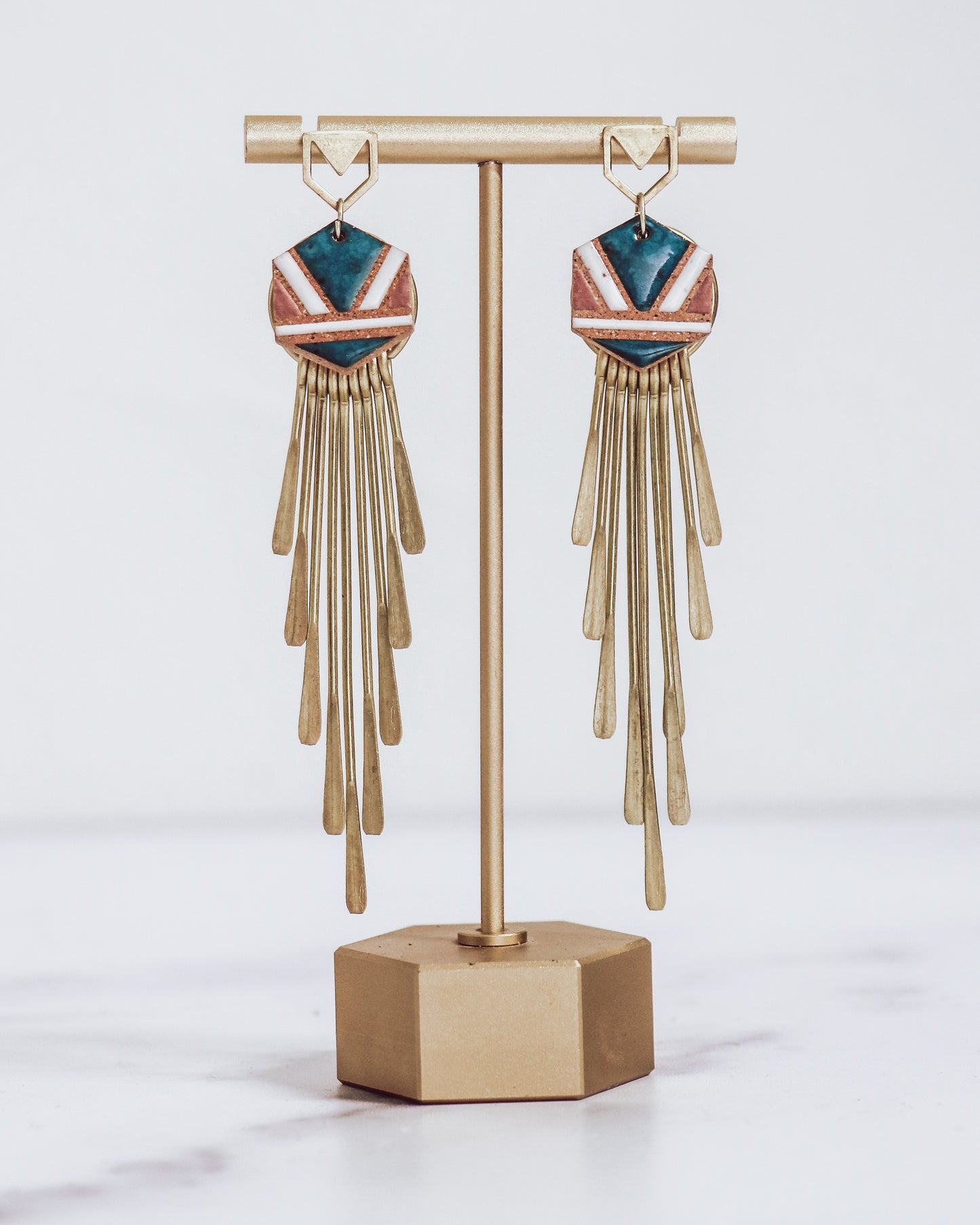Long gold fringe tassel earrings with hexagon-shaped ceramic tops, shown in "nicola" glaze pattern  a gold stand.