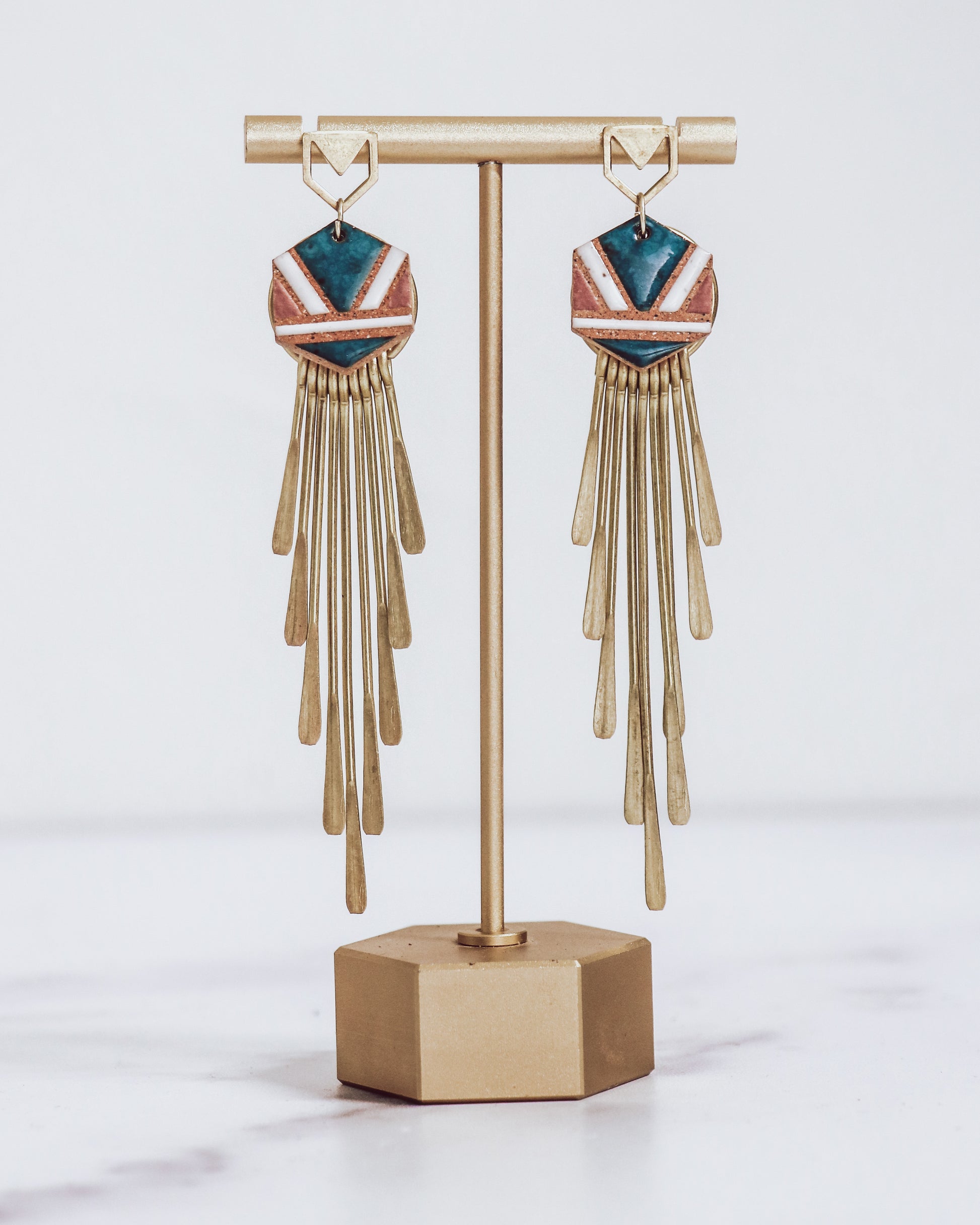 Long gold fringe tassel earrings with hexagon-shaped ceramic tops, shown in "nicola" glaze pattern  a gold stand.