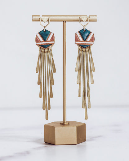 Long gold fringe tassel earrings with hexagon-shaped ceramic tops, shown in "nicola" glaze pattern  a gold stand.