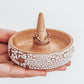 Ceramic ring holder with center cone, crackle white exterior, and speckled tan interior, shown in hand with rings for scale.