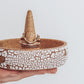Close up of Ceramic ring holder with center cone, crackle white exterior, and speckled tan interior, shown in hand with rings for scale.