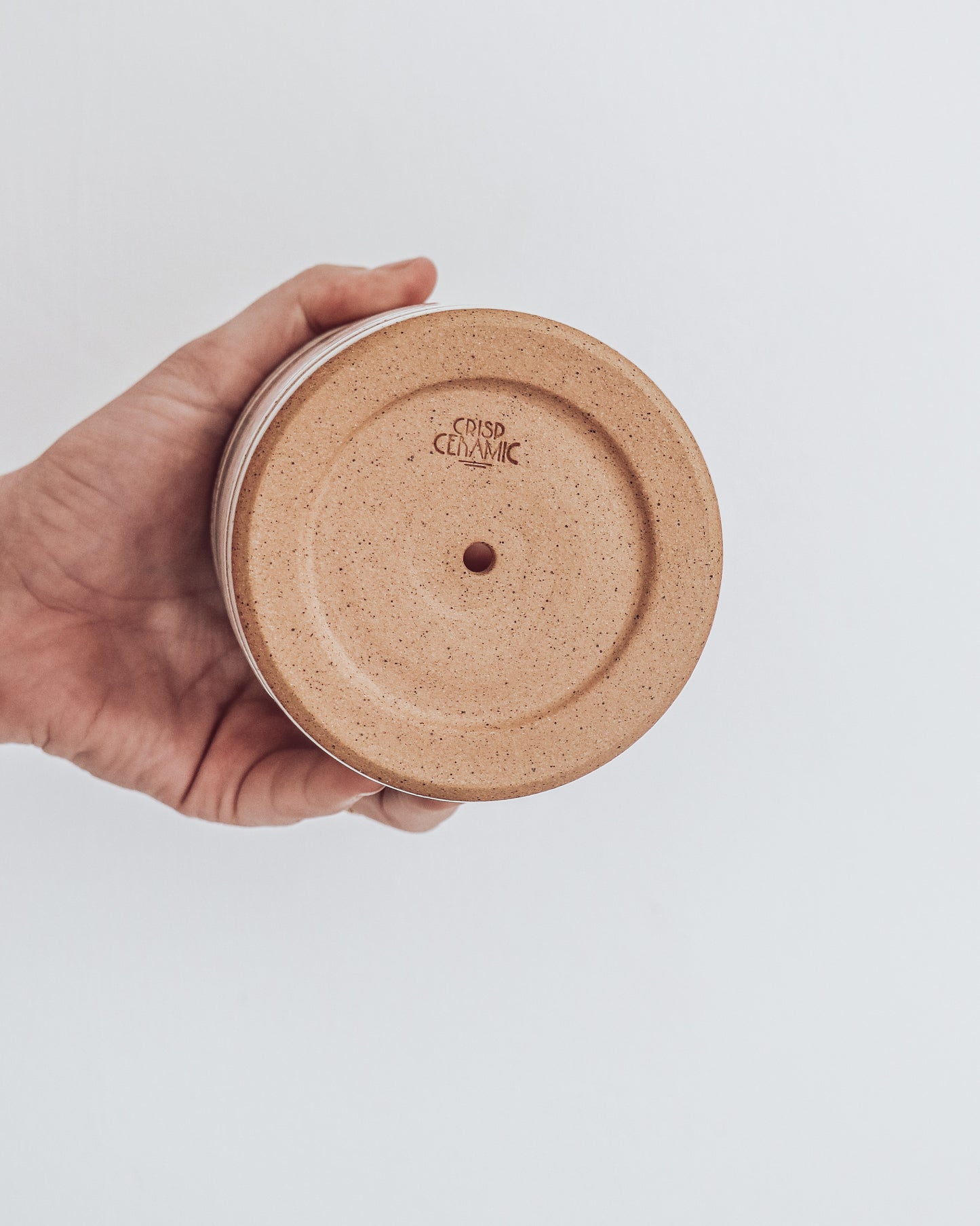 Bottom View of Art Deco Planter in white speckled glaze with geometric detailing, shown held in hand for scale. Bottom of planter is unglazed.