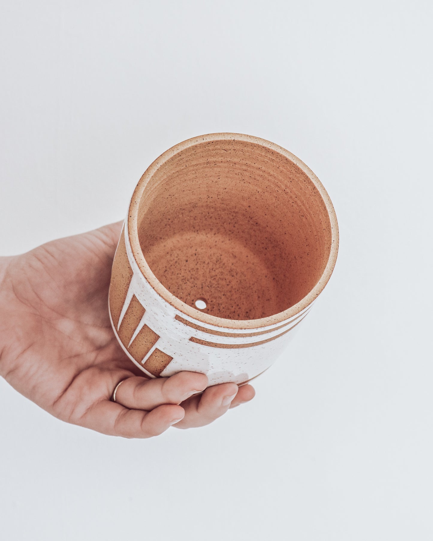 Inside view of Art Deco Planter in white speckled glaze with geometric detailing, shown held in hand for scale. Inside of planter is unglazed. 
