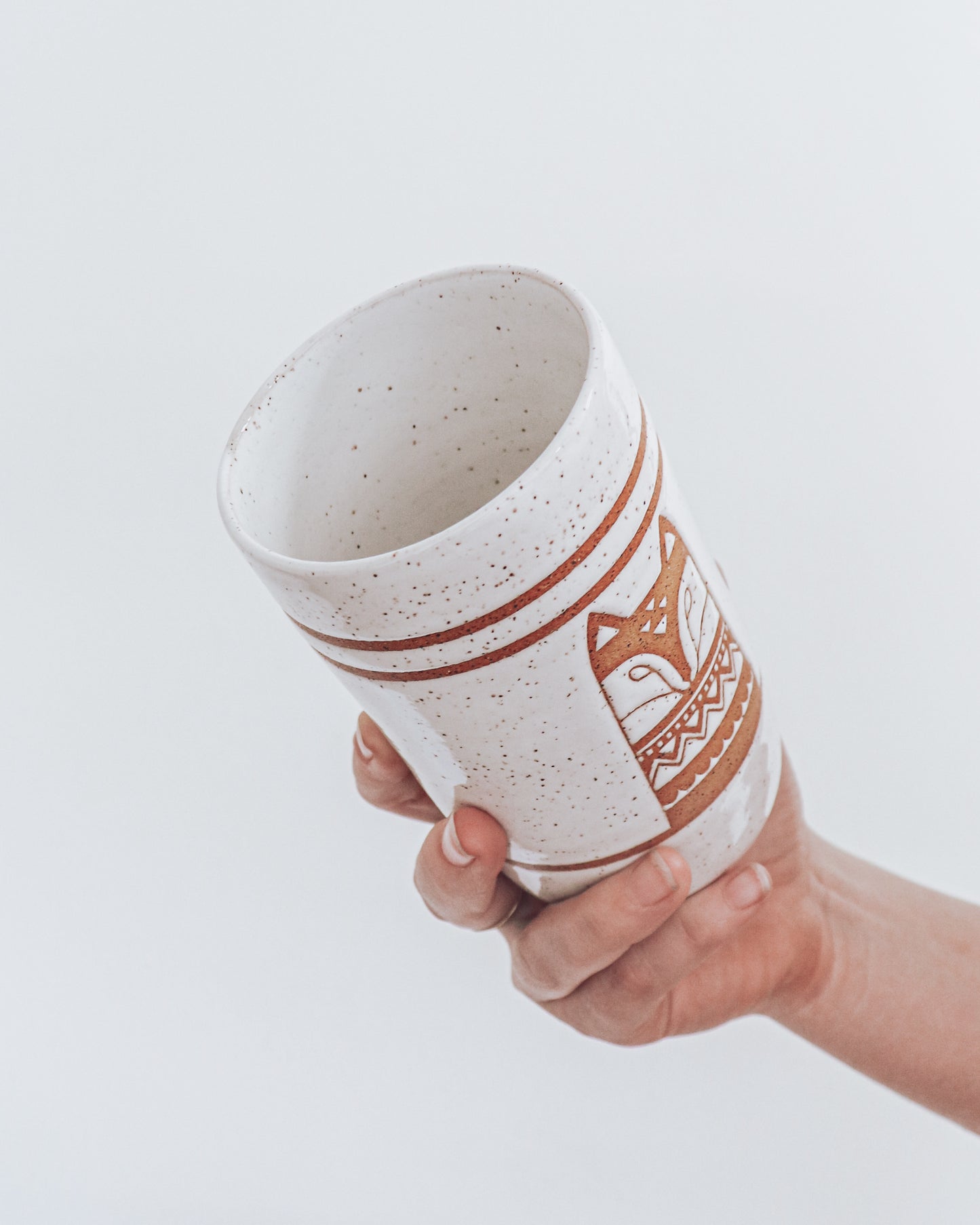 A ceramic fox-shaped tumbler with a glossy white glaze, held in a person's hand against a white background.