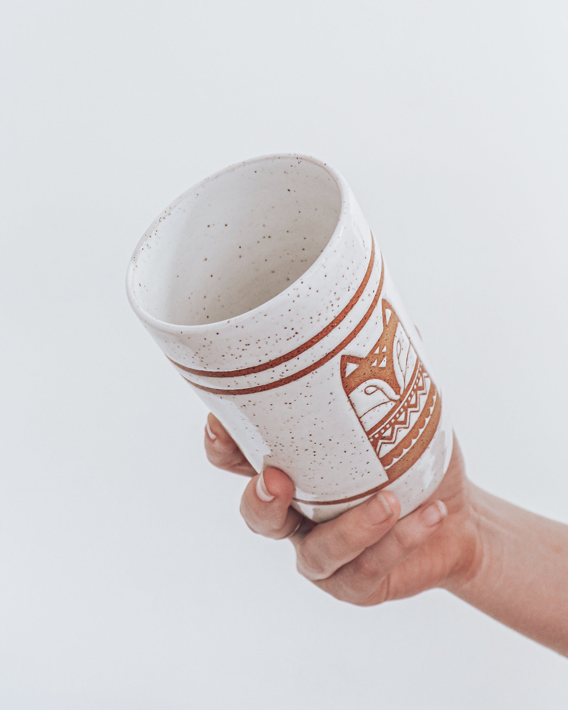A ceramic fox-shaped tumbler with a glossy white glaze, held in a person's hand against a white background.