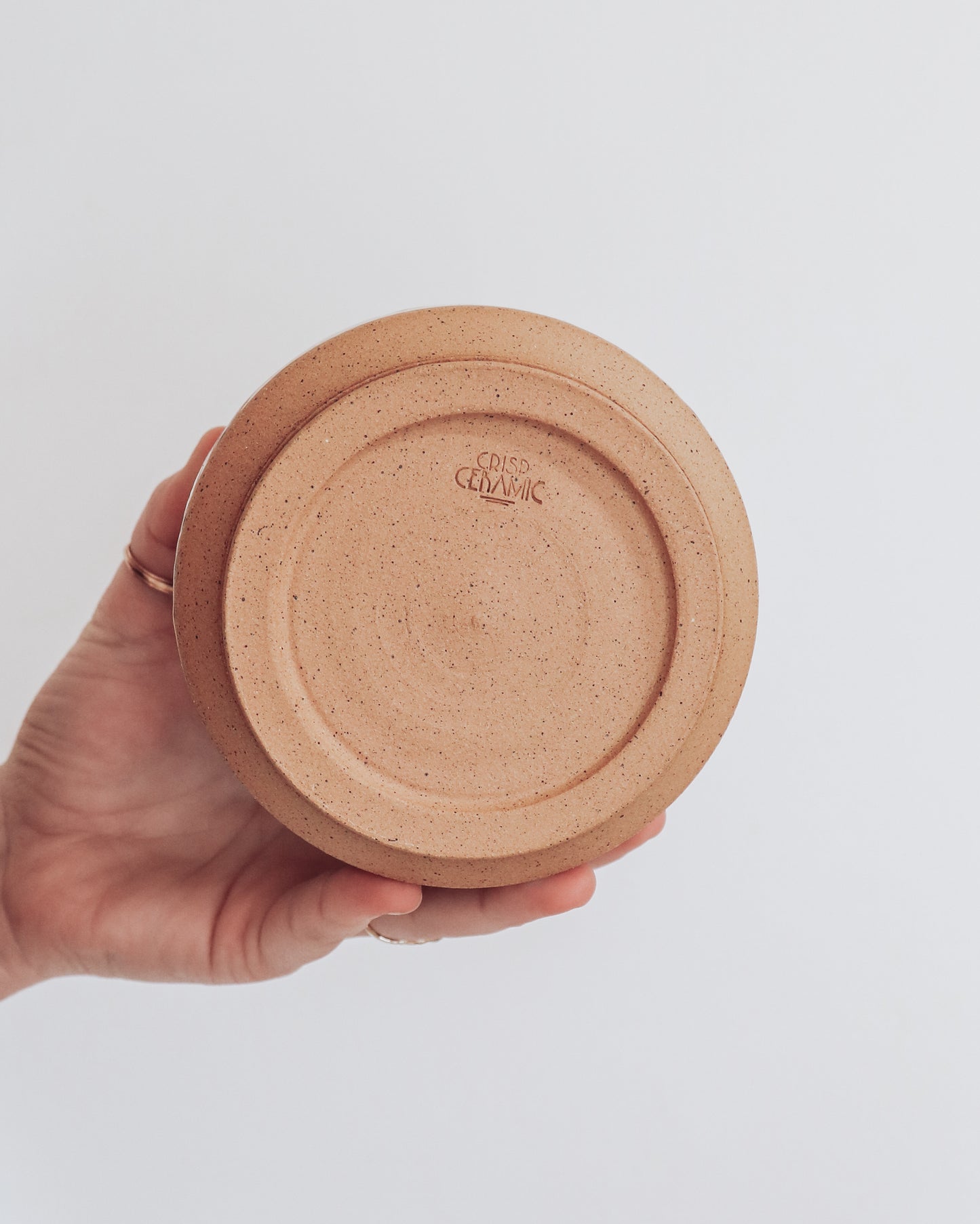 Hand holding a handmade ceramic planter with white glaze and wavy multicolored stripe detailing. Shows unglazed base with crisp ceramic makers mark. 