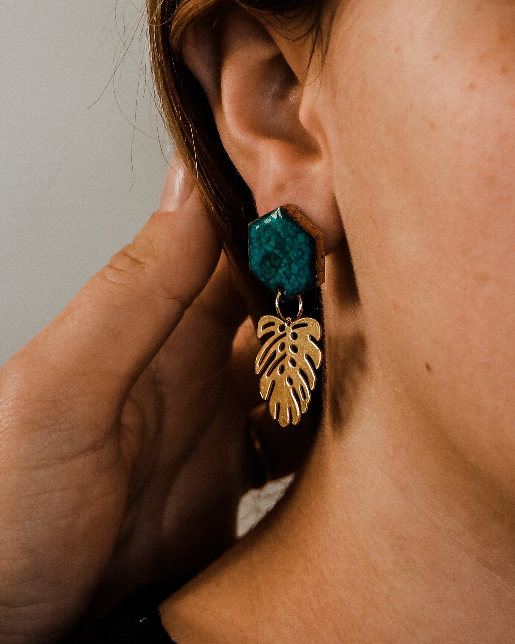 Handmade ceramic and brass monstera leaf earrings shown in green on a model