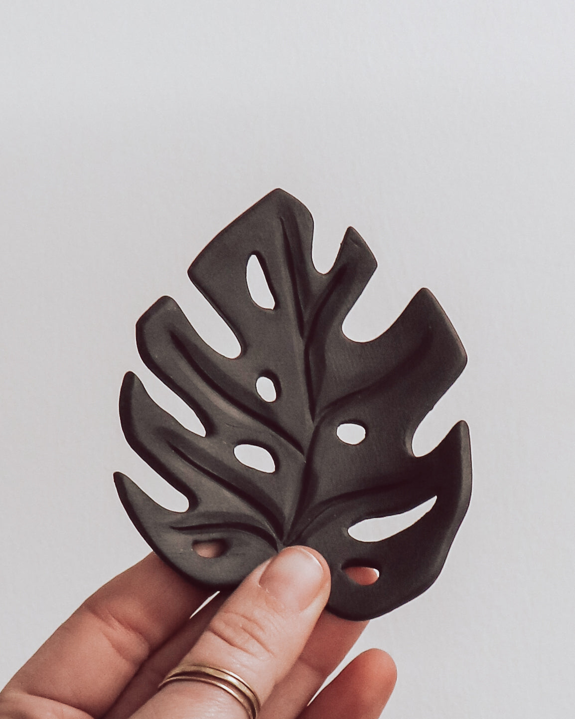 A ceramic leaf-shaped plate in a slate color, held between fingers, with a textured surface.