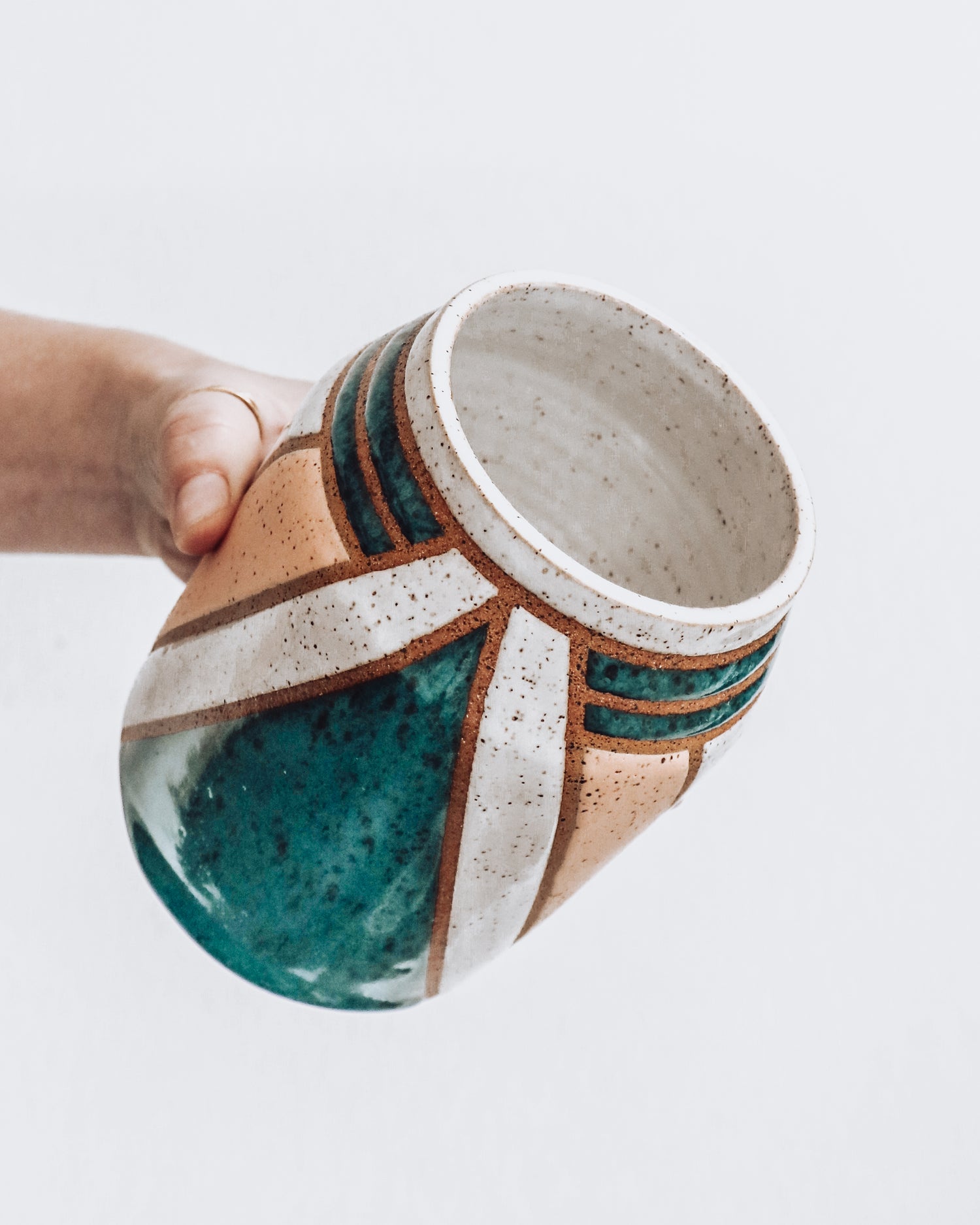 Handmade Nicola Vase featuring emerald green glaze accents, geometric detailing, and speckled white lines. Vase is being held at an angle. 