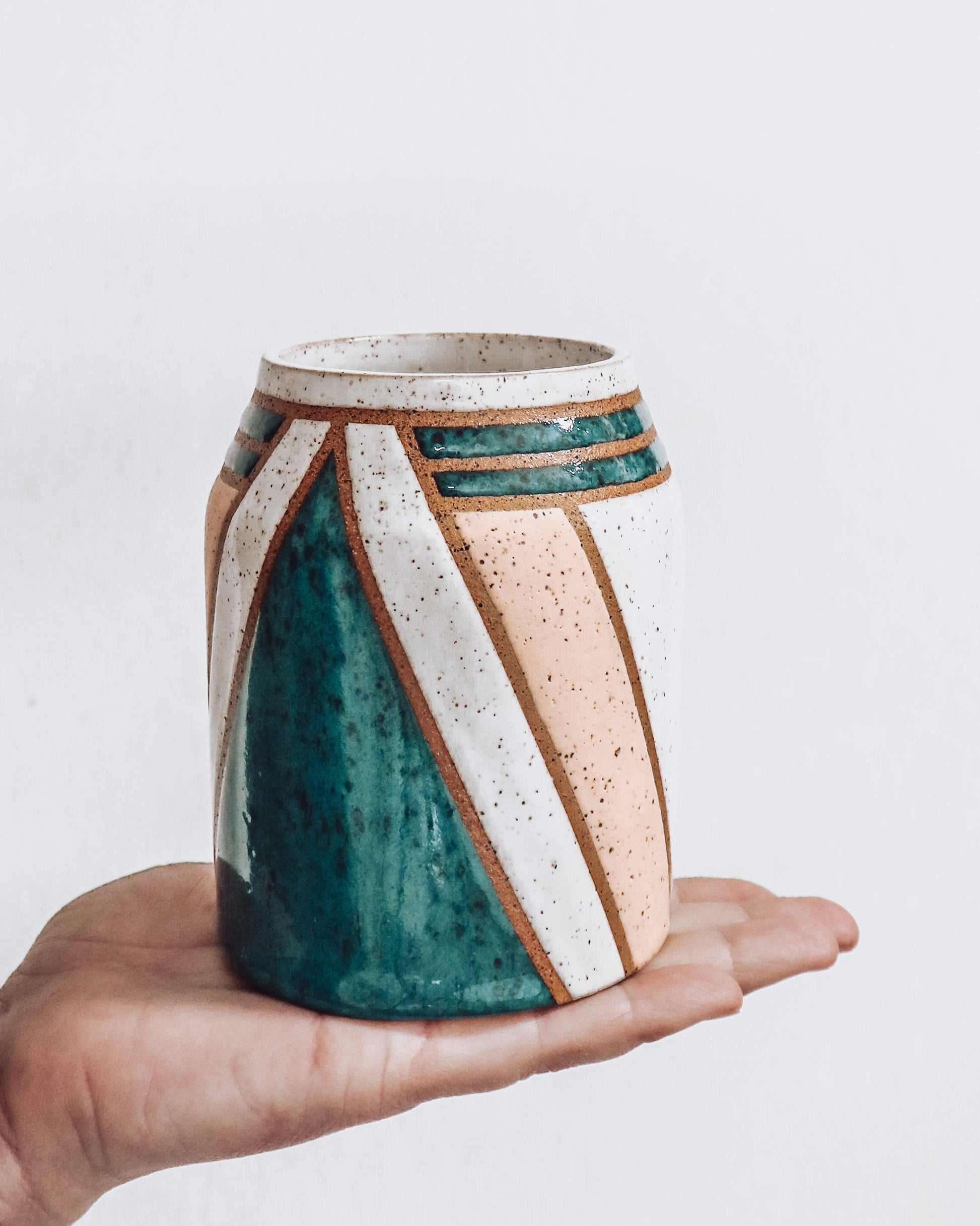 hand holding a handmade ceramic vase featuring teal, white and pink glaze with geometric pattern.