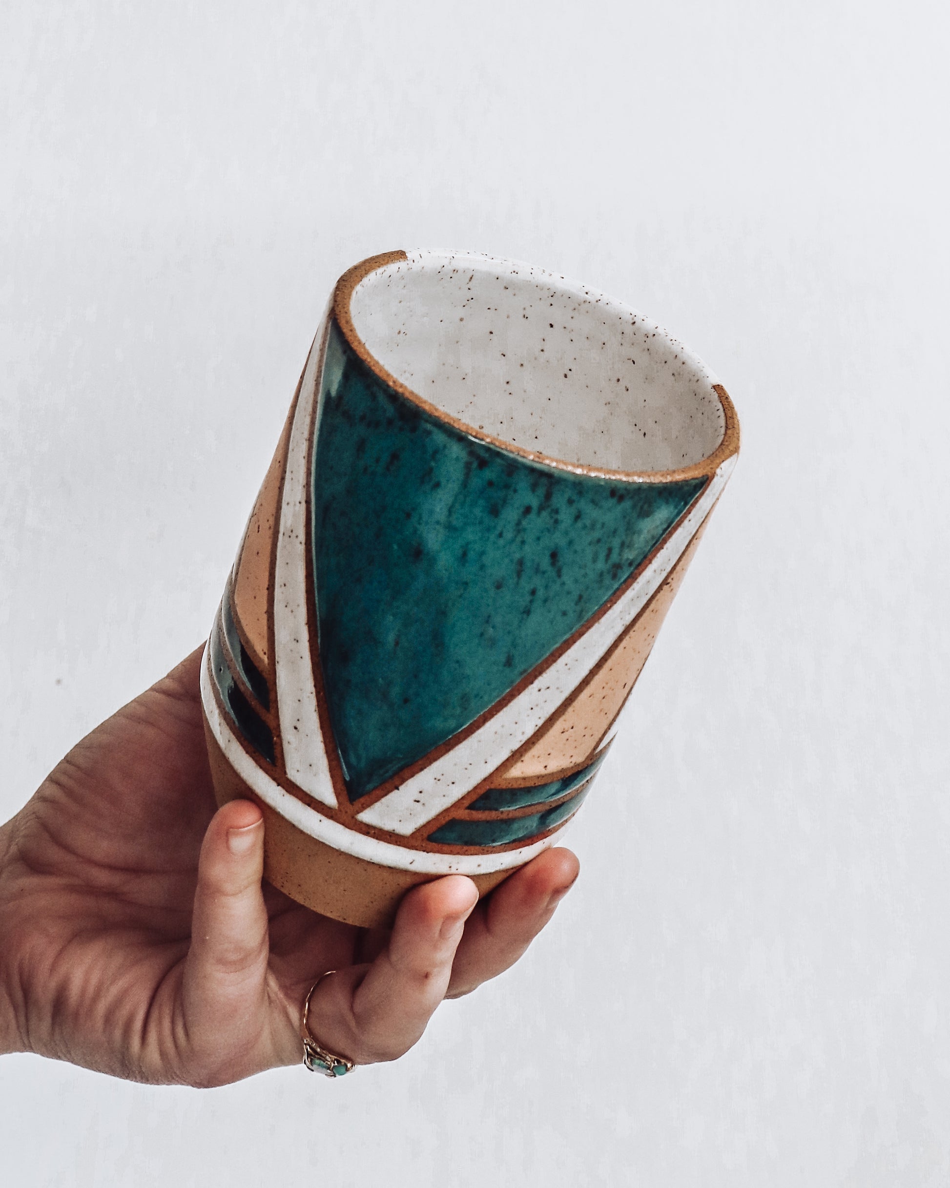 hand holding a handmade ceramic vase featuring teal, white and pink glaze with geometric pattern.