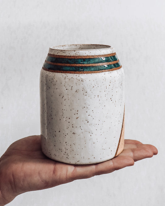 hand holding a handmade ceramic vase featuring (back view) showing green stripes and white back of vase.