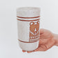 Hand Holding a handmade speckled ceramic tumbler featuring a brown illustrated bear design with geometric detailing. 