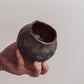 A ceramic 'boulder' planter or vase with a matte charcoal glaze, held in a person's hand.