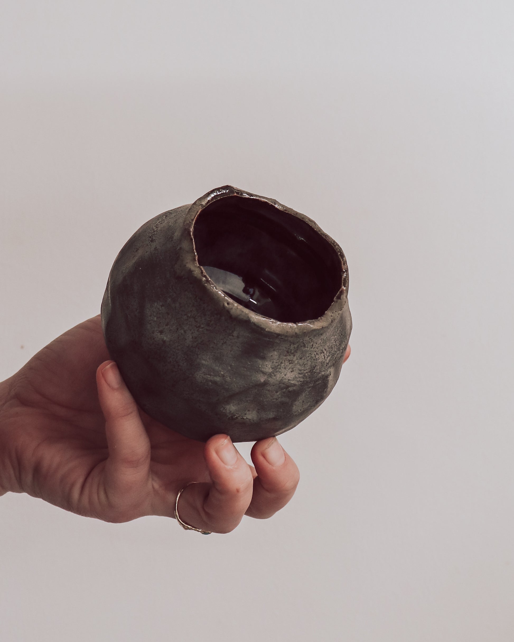 A ceramic 'boulder' planter or vase with a matte charcoal glaze, held in a person's hand.