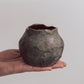 A ceramic 'boulder' planter or vase with a matte charcoal glaze, held in a person's hand.