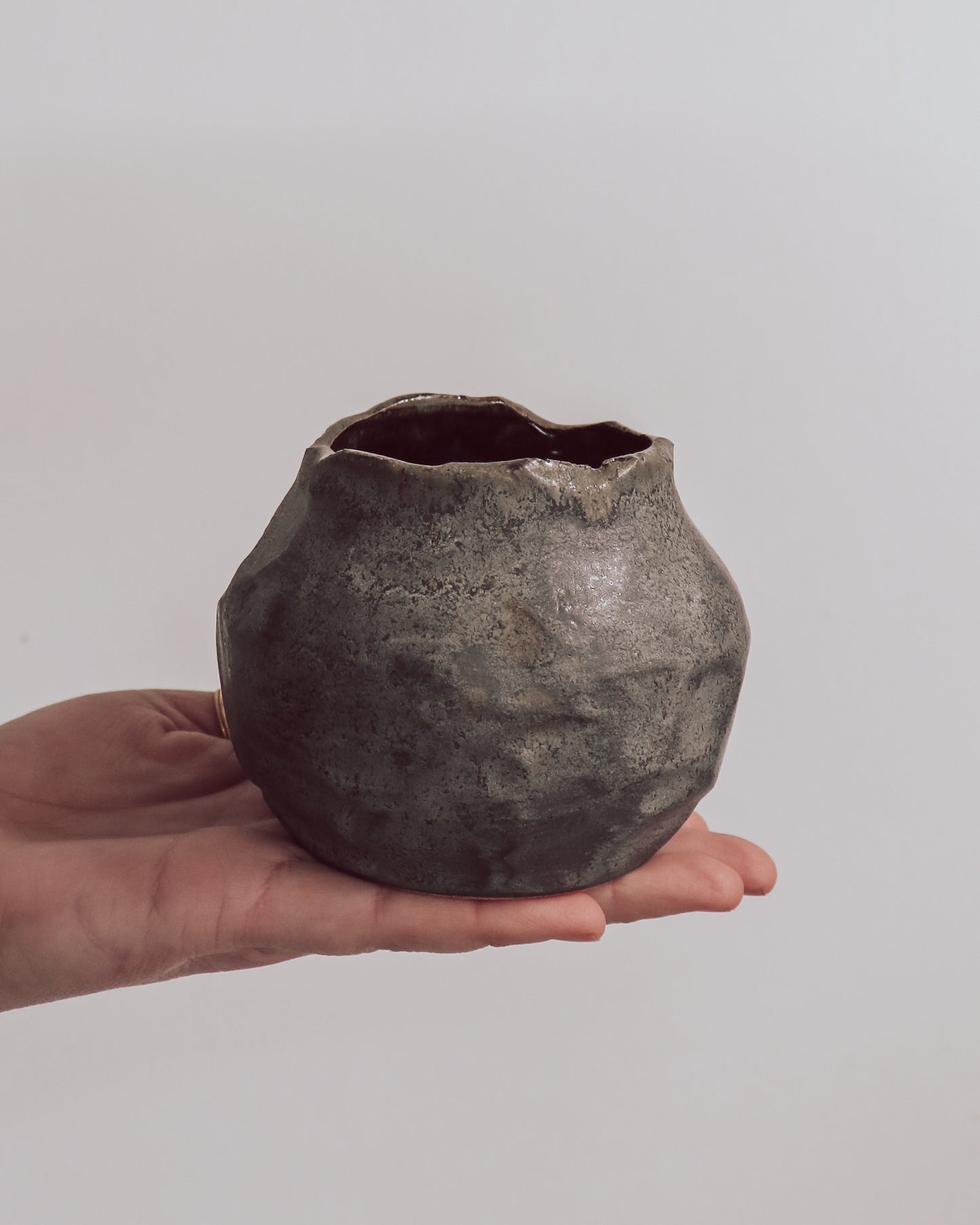 A ceramic 'boulder' planter or vase with a matte charcoal glaze, held in a person's hand.
