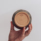 A ceramic 'boulder' planter or vase with a matte charcoal glaze, held in a person's hand showing crisp ceramic makers mark.