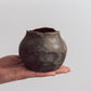 A ceramic 'boulder' planter or vase with a matte charcoal glaze, held in a person's hand.