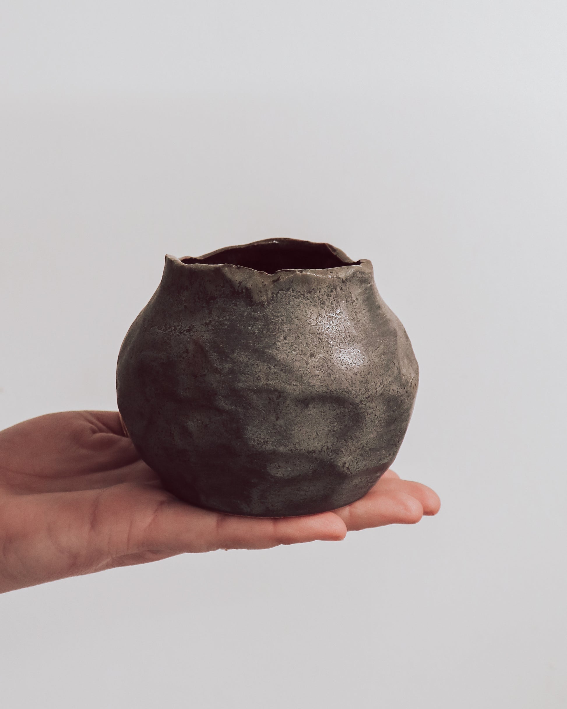 A ceramic 'boulder' planter or vase with a matte charcoal glaze, held in a person's hand.